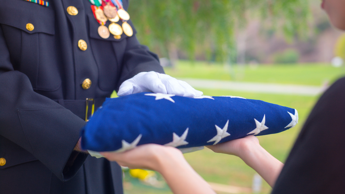 Gloved hands pass a folded flag to a family member