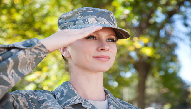 A man in uniform playing military bugle in front of American flag